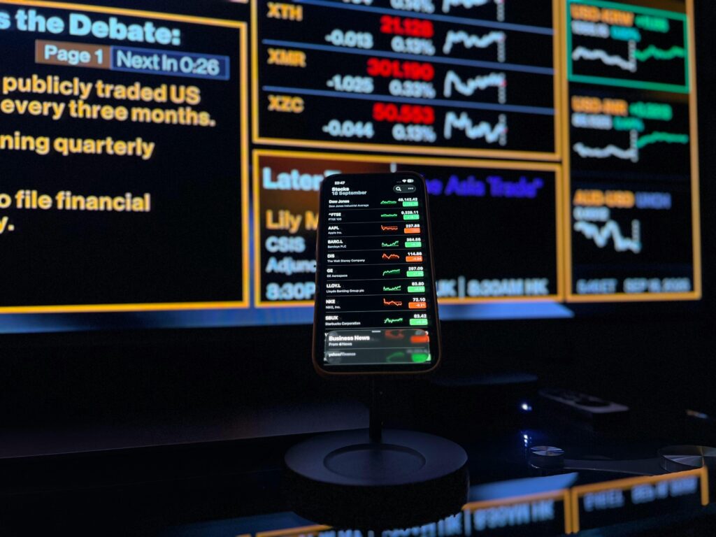 Smartphone displaying stock market data against financial screen backdrop in London.
