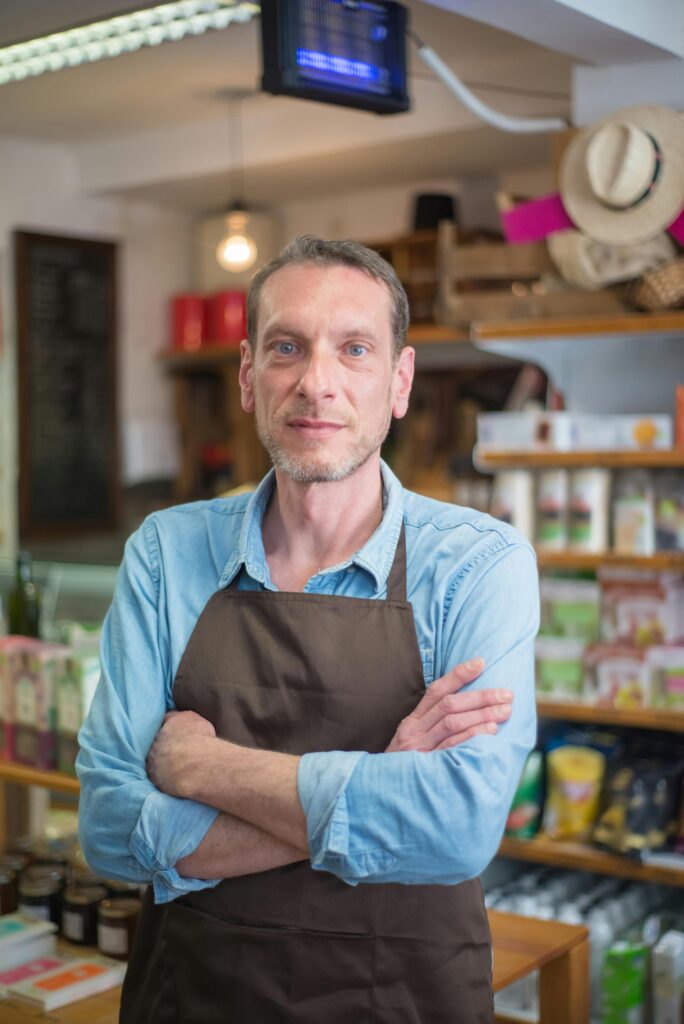 Confident male shop owner with arms crossed in a rustic village store, Portugal.
